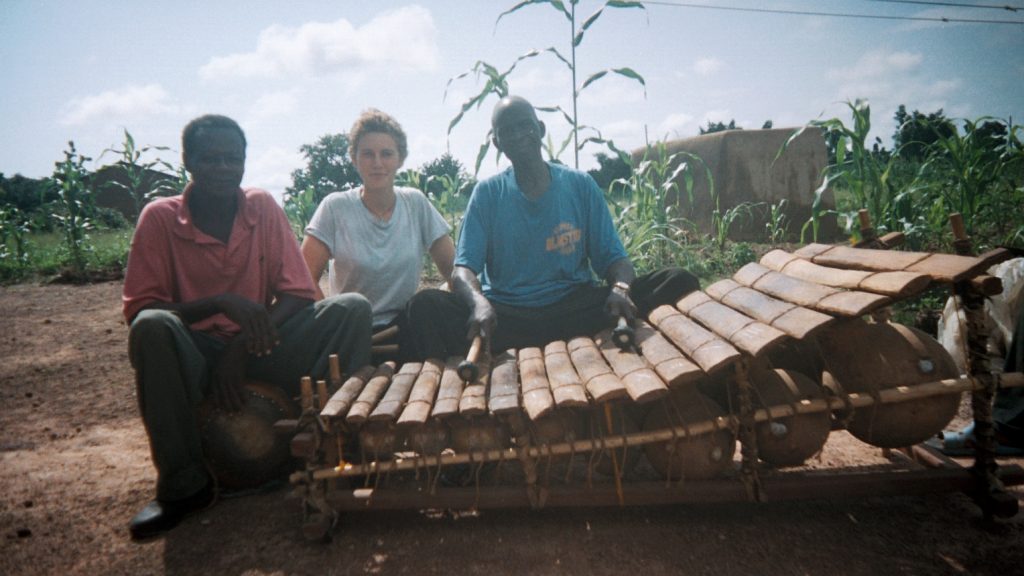 Bex Burch (middle) and Thomas Sekgura (right), taken when Bex was his apprentice, sitting behind the gyil, in their compound in Guo